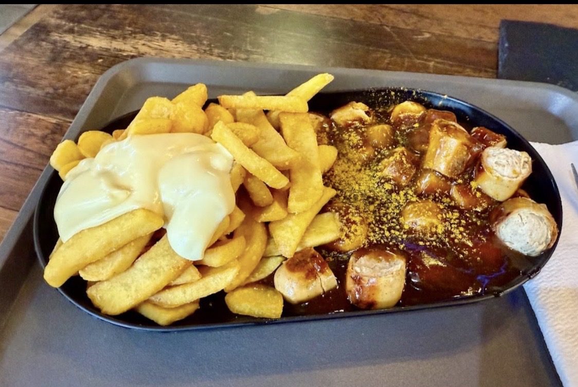 Currywurst mit Currysoße und Pommes mit Mayo auf einem schwarzen Teller