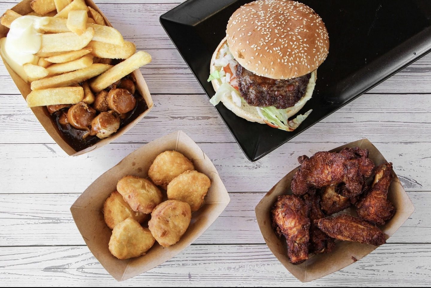 Burger, Chicken Nuggets und Pommes Currywurst in Pappschalen auf Holz