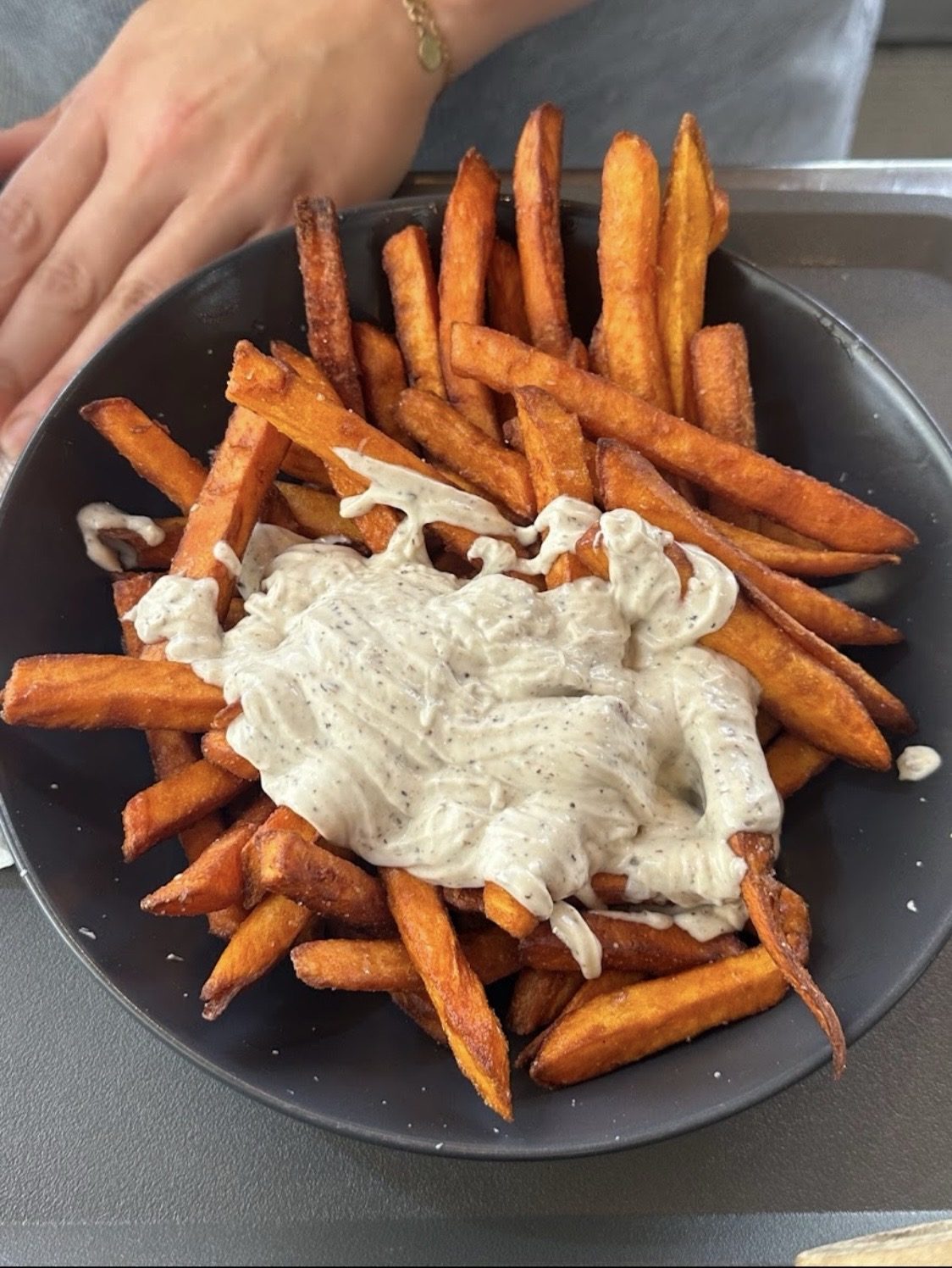 Süßkartoffel-Pommes mit heller Soße in einer schwarzen Schale